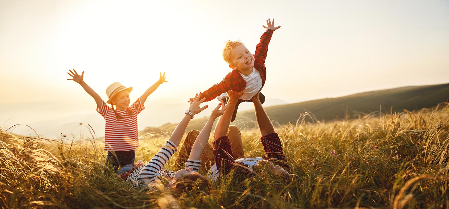 Adult couple with two children in a field of tall grass at sunset.